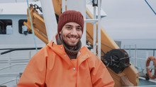 Portrait Of Dressed In Bright Protective Coat Smiling On Camera Fisherman On Commercial Fishing Boat.