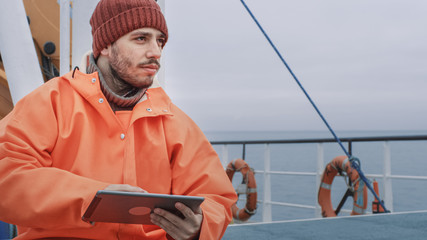 Dressed in Protective Coat Fisherman Using Tablet Computer with Navigation Maps while Traveling on Ship.