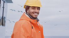 Portrait Of Dressed In Bright Protective Coat Smiling Fisherman On Commercial Fishing Boat.