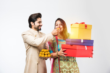 Wall Mural - Indian couple with laddu and gift boxes on diwali /festival, standing isolated over white background. wearing traditional cloths