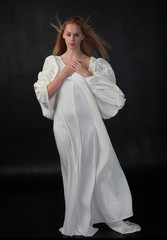 Poster - full length portrait of blonde girl wearing long white flowing robe. standing pose against a black studio background.