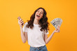 © Drobot Dean - Pleased happy smiling young woman posing isolated over yellow wall background using mobile phone holding money.