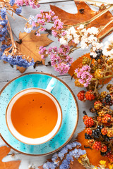 composition still life of a mug with hot leaf tea with berries and autumn leaves on a wooden surface