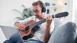 © astrosystem - Man playing acoustic guitar in the living room.