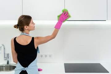 Young adult woman cleaning kitchen cabinet at home