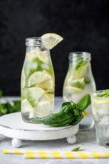 Wall Mural - Summer basil lemonade on grey background. Fresh summer cocktail with basil, lemon and ice cubes. Homemade fresh lemonade with lemon and basil. Food and drink concept