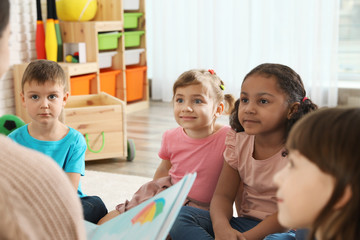 Poster - Kindergarten teacher reading book to cute little children indoors