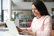 © New Africa - Young happy woman using laptop at table in library
