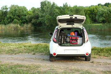 Car with camping equipment in trunk on riverbank. Space for text