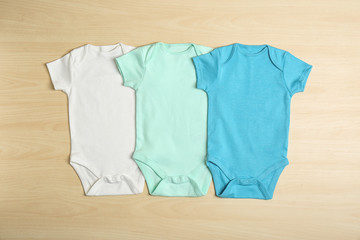 Different baby bodysuits on wooden background, top view