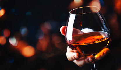 French glowing cognac glass in hand on the dark bar counter background, copy space, selective focus