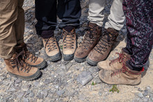 Company Four Tourists Only Legs Together In Brown Trekking Hiking Boots With Laces On Rocky Cliff. Concept Freedom, Travel Lifestyle Adventure Vacations, Traveler Outdoor Wild Nature Summer Steps