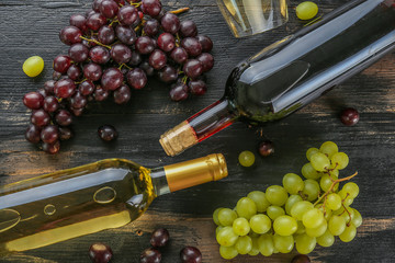 Two bottles with red and white wine with blank matte label with bunches of different type grapes and wineglass on grunged wooden texture table. Background, copy space, flat lay, cose up, top view.