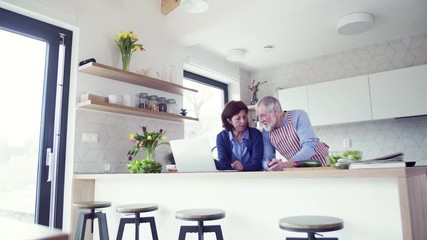 Poster - A portrait of senior couple with laptop indoors at home, cooking.