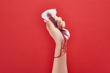 Wall Mural - partial view of woman squeezing sanitary towel with blood on red background