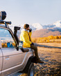 © Sibstock/Stocksy - Young hipster guy in stylish clothes is sitting on the hood of a jeep and drinking hot tea. Heats and rests, took a break on a long journey.