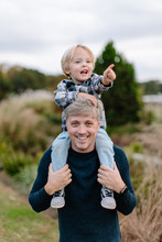 Adorable Young Boy Sitting On His Father's Shoulders Pointing To Something