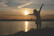 © Natali - Silhouette of young dancing woman in sunset rays on a lake shore.