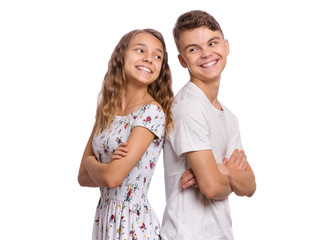 Wall Mural - Portrait of smiling teen boy and girl standing back to back. Teenagers look at each other. Happy children in casual clothes with folded arms, isolated on white background. Friendship and love concept.