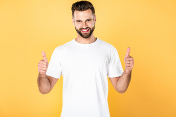 happy handsome man in white t-shirt showing thumbs up isolated on yellow