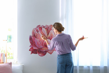 Poster - Young interior designer painting flower on wall in modern room