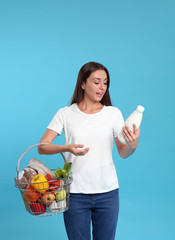 Wall Mural - Young woman with shopping basket full of products on blue background