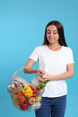 Wall Mural - Young woman with shopping basket full of products on blue background