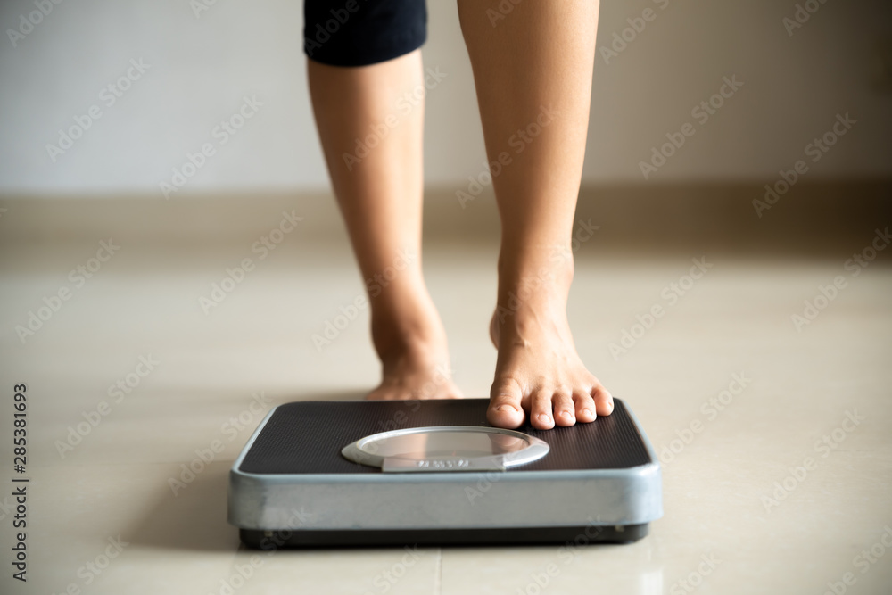 Female leg stepping on weigh scales. Healthy lifestyle, food and sport concept. - obrazy, fototapety, plakaty 