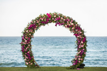 Wedding Round Arch Decorated With Beautiful Colorful Orchid And Rose Flowers On The Beach. Ocean On Background.