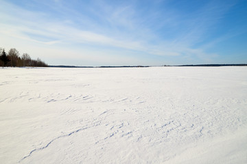 Winter landscape with snow covered field and blue sky with clouds