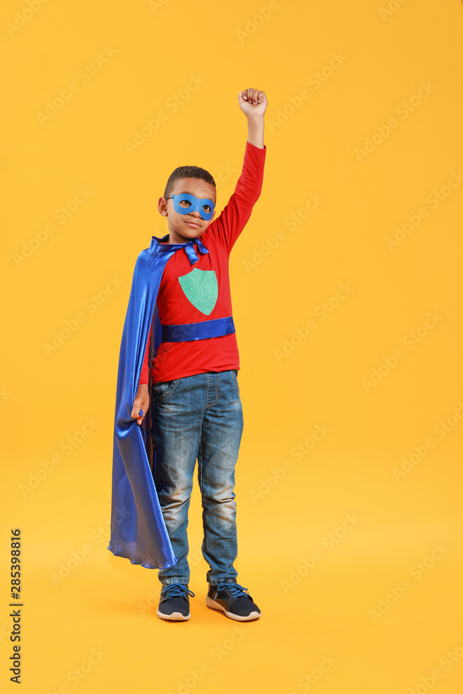 Cute African-American boy dressed as superhero on color background
