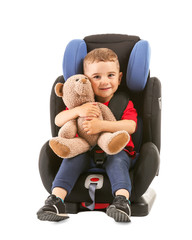 Canvas Print - Little boy with toy bear buckled in car seat on white background