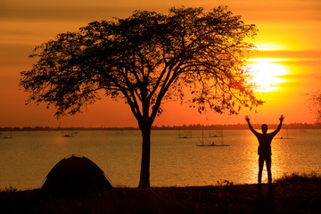 Wall Mural - The silhouette of the sunset, the lake, people spread their hands over the head, tourists tents, tourists with sunrise or sunset.