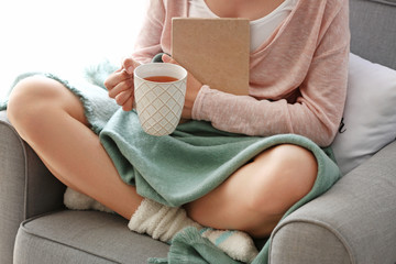 Young woman with book drinking hot tea at home