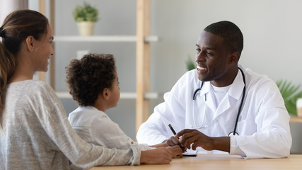 Wall Mural - Smiling black male doctor listening to little patient make notes