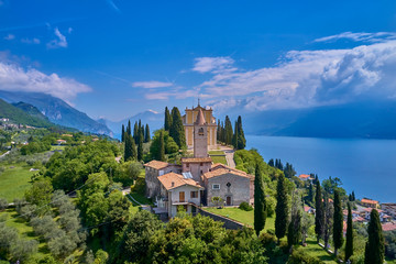 The resort town of Pulciano, located on the shores of Lake Garda. San Michele Arcangelo Church is located on a mountain. Panoramic view of the city, church, Lake Garda, Alps. Aerial view.