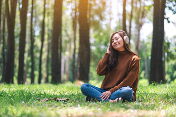 Wall Mural - A beautiful asian woman enjoy listening to music with headphone with feeling happy and relaxed in the park