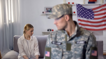 Wall Mural - Angry wife sitting on sofa, military husband on foreground, misunderstanding