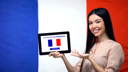 Lady holding tablet with learn French app, France flag on background, education