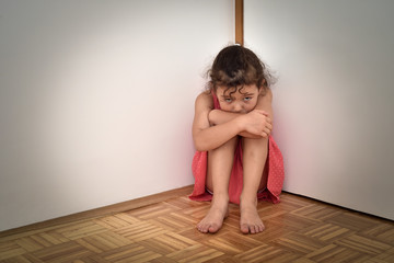 sad and unhappy young girl sitting on the floor in the empty room, embracing her knees and looking a