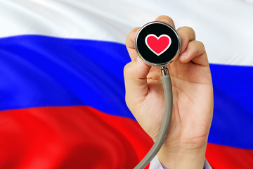 Doctor holding stethoscope with red love heart. National Russia flag background. Healthcare system concept, medical theme.