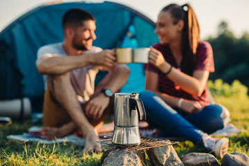 Wall Mural - young couple on camping by the river , making a toast with coffee or tea