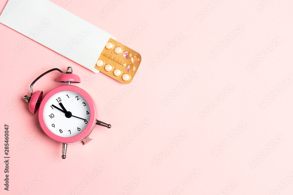 Female oral contraceptive pills blister with alarm clock on pink background. Women contraceptive hormonal birth control pills. - obrazy, fototapety, plakaty 