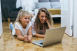 © cherryandbees - mother and daughter laying on the floor at home and using computer