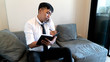 © SVRSLYIMAGES - Asian Businessman talking on mobile phone while working on notebook at his living room sofa