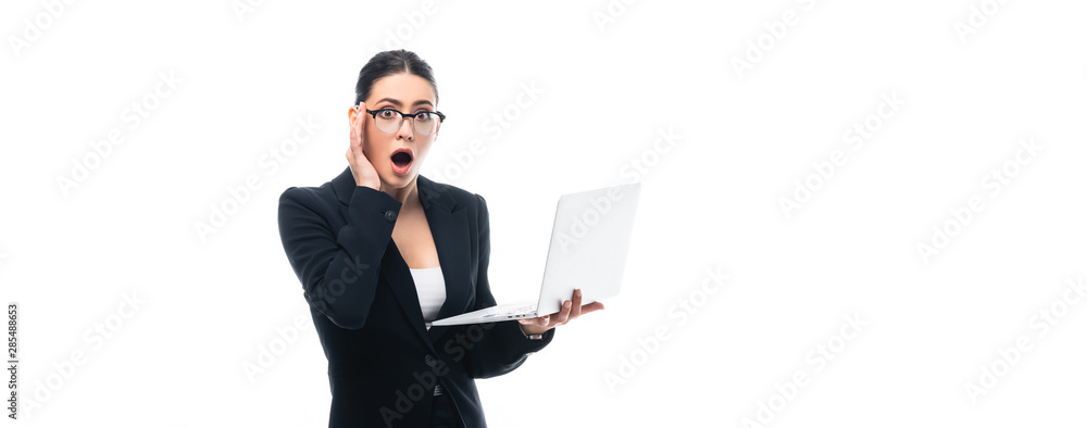 Fotografia panoramic shot of shocked businesswoman holding laptop while looking at camera i