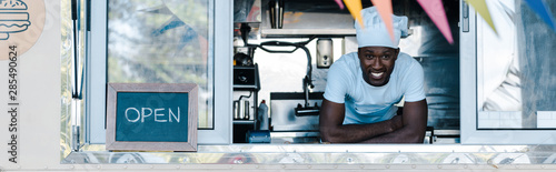 Fotografía panoramic shot of happy african american man in chef uniform smiling from food t