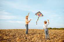Father With Son Launching Colorful Air Kite On The Field. Concept Of A Happy Family Having Fun During The Summer Activity