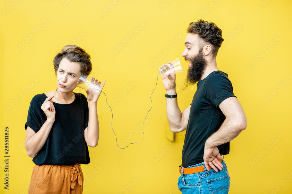 Man and woman talking with string phone made of cups on the yellow background. Concept of communication - obrazy, fototapety, plakaty 
