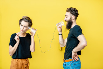 man and woman talking with string phone made of cups on the yellow background. concept of communicat